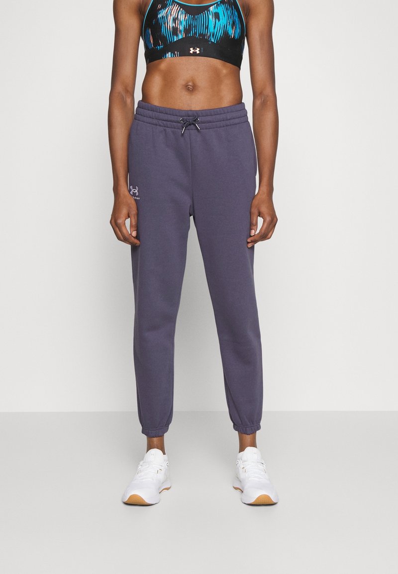 Lilla joggingbukser med elastiske manchetter, snor i taljen og logo-detail på venstre ben, parret med en multikolor sports-BH og hvide sneakers.