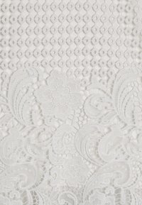 Vitt spetstyg med cirkulära och blommiga mönster med en texturerad yta, som visar upp intrikata detaljer och fin hantverksskicklighet.