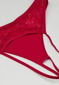 Czerwona bielizna z gładkiego materiału z koronkowymi akcentami na pasie, trójkątnym kształcie i cienkimi regulowanymi ramiączkami.