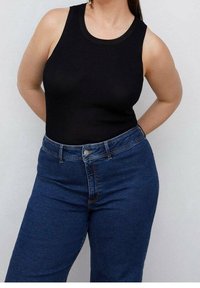 Top negro de canalé con escote redondo combinado con unos vaqueros de cintura alta en color azul. Los vaqueros tienen un cierre frontal con botón y cremallera.