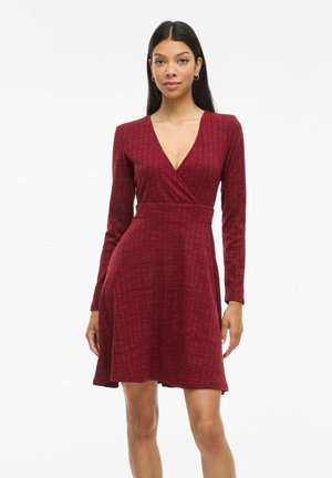 Robe rouge à manches longues avec un décolleté en V profond et un design enveloppant. Tissu texturé avec un motif à carreaux subtil, évasée à partir de la taille.