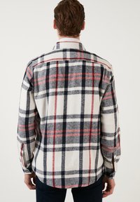 Geverfd flanellen overhemd in wit, marineblauw en rood. Kenmerkt zich door een knoopsluiting aan de voorkant, lange mouwen en zijsplitten aan de onderkant. Gelaagd materiaal.