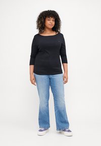 Svart langermet topp med bred hals, parret med lyseblå, utsvingte jeans og lilla joggesko. Glatt stoff, uformelt design.