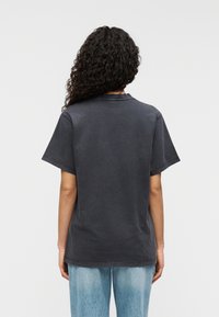 Μαύρο-γκρι βαμβακερό μπλουζάκι με κοντά μανίκια, χαλαρή γραμμή και στρογγυλή λαιμόκοψη. Ορατή ραφή προσθέτει λεπτομέρε ια. Φορεμένο με ανοιχτόχρωμο τζιν.