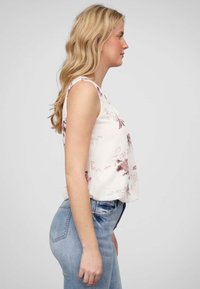 Top floral sans manches en crème avec des motifs roses, associé à un jean taille haute bleu. Tissu doux, coupe décontractée et détail de couture sur le côté visible.