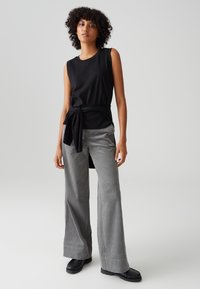 Black sleeveless top with a tied waist, paired with light gray wide-leg pants made of textured fabric, worn with black footwear.