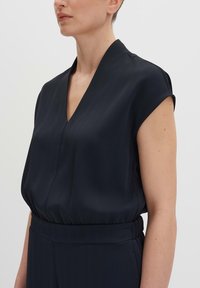 Donker marineblauw mouwloos topje met een V-hals en geplooide textuur. Heeft een gatherde taille en zacht materiaal voor een relaxte pasvorm.