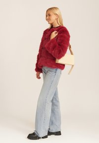 Crimson faux fur oversized sweater with long sleeves, paired with light blue flared jeans and black chunky boots. Holds a tan crossbody bag.
