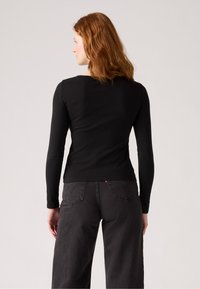 Svart langermet skjorte med en tettsittende design, glatt tekstur og rund hals, kombinert med høy midje mørke jeans.
