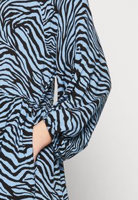 Tissu imprimé zèbre bleu et noir avec une coupe décontractée. Comprend des manches longues et une taille froncée. Texture douce, mettant en avant un motif audacieux.