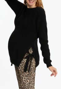 Schwarzer Strickpullover mit langen Ärmeln und seitlichen Schlitzen, kombiniert mit Leoprint-Hosen mit gebundenen Akzenten. Weiche Textur überall.