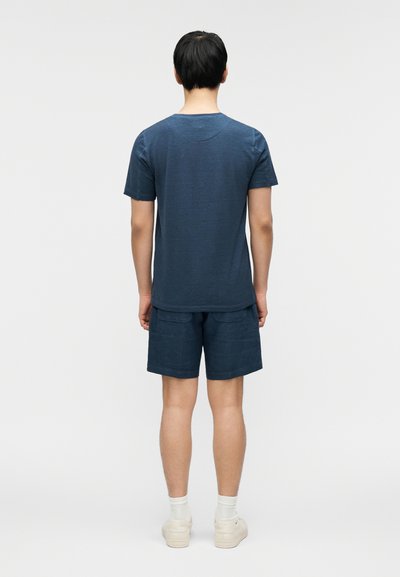 Μπλε ναυτικό μπλουζάκι και αντίστοιχα σορτς κατασκευασμένα από ελαφρύ ύφασμα. Απλός σχεδιασμός με κοντά μανίκια και χαλαρή εφαρμογή. Χωρίς ορατά σχέδια.
