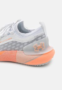 Chaussure de running Under Armour Phantom blanche et orange avec tige en mesh, col semblable à une chaussette et logo sur le contrefort du talon.