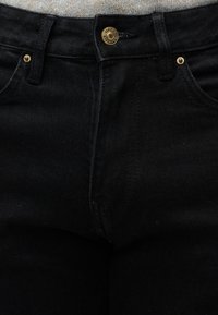 Μαύρο τζιν από ντένιμ με ψηλή μέση, που διαθέτει χρυσά μεταλλικά στοιχεία, πέντε τσέπες και αντίθετη ραφή στις ενώσεις. Υφή υφάσματος με ελαφριά ελαστικότητα.