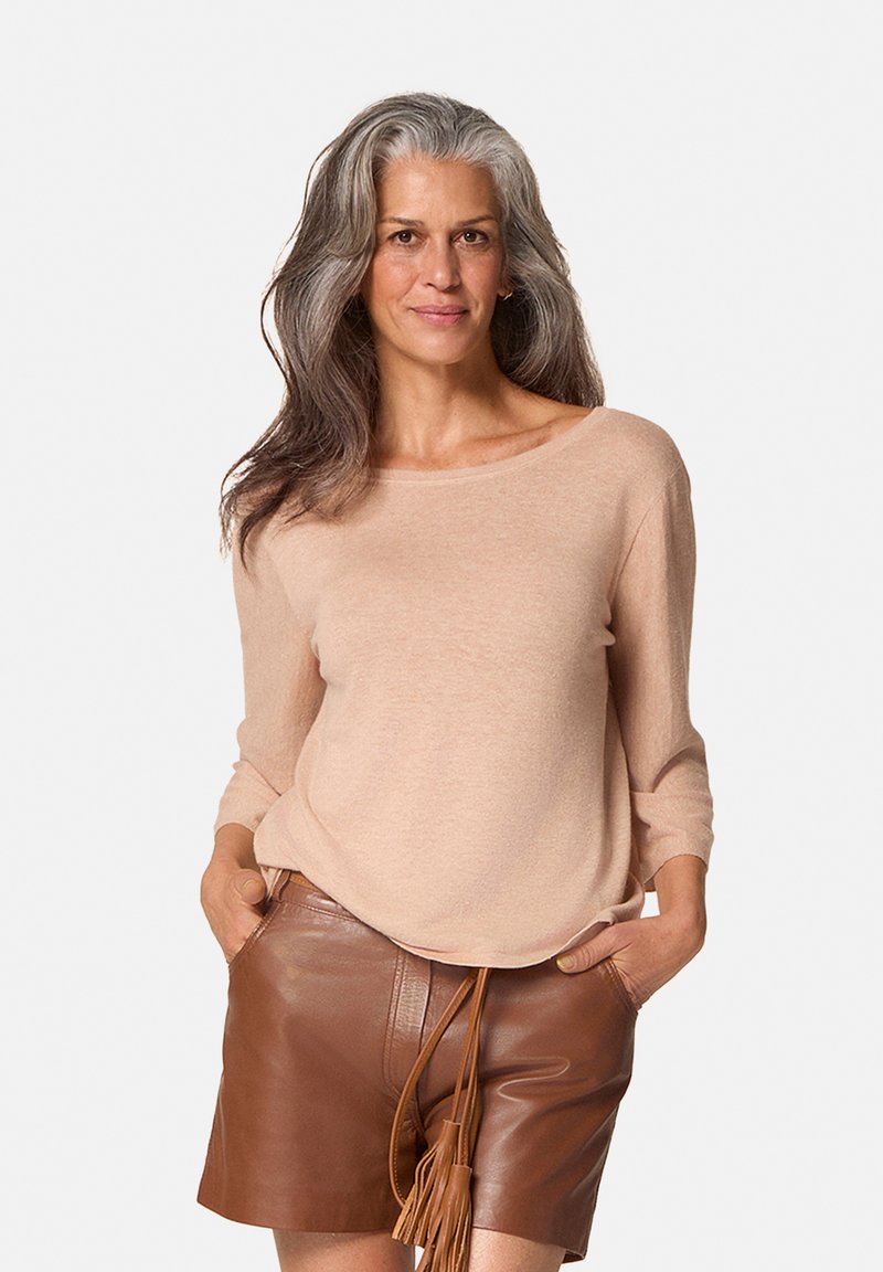 Lichtbeige lange mouw gebreide trui met een brede halslijn, gedragen met bruine leren shorts met een franje trekkoord. 