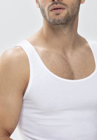 Biały top na ramiączkach wykonany z gładkiego materiału, z okrągłym dekoltem i cienkimi ramiączkami, zaprezentowany na neutralnym tle.