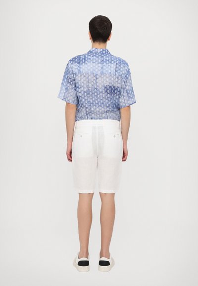 Chemise à manches courtes bleue à motifs et shorts en lin blancs. La chemise présente une texture subtile, tandis que les shorts sont taillés avec des poches arrière.