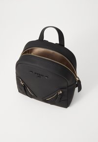 Sac à dos synthétique noir avec des zips dorés, en forme arrondie, deux poches avant zippées et des détails de logo. Texture lisse avec une petite poignée sur le dessus.