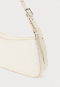 Crème handtas met een gladde afwerking, geometrisch patroon en een dunne verstelbare schouderband. Voorzien van een zilveren sluiting en een zachte textuur.