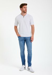 Polo de manga corta gris claro con un patrón geométrico texturizado, llevado con jeans azules y zapatillas blancas con un acento negro.