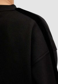 Felpa nera con tessuto testurizzato, collo rotondo e pannello in velluto nero a contrasto sulla spalla con dettagli di cuciture visibili.