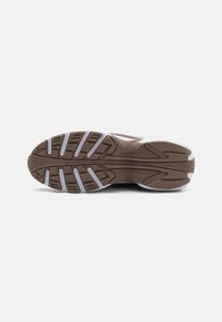 Semelle de chaussure de sport marron avec une surface en caoutchouc texturé, des crampons proéminents pour l'adhérence et des accents blancs le long des bords.