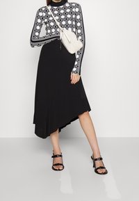 Falda negra asimétrica con un top de manga larga en blanco y negro con estampado. El top presenta diseños geométricos y mangas estructuradas.