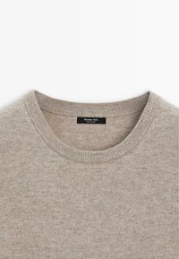 Pullover beige lavorato a maglia con scollatura rotonda e bordo a coste. Texture morbida e etichetta con la scritta "Massimo Dutti" attaccata all'interno.