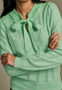 Pull en maille vert menthe avec fermeture à nouer, rayures texturées et manches bouffantes, fabriqué dans un tissu doux et léger.
