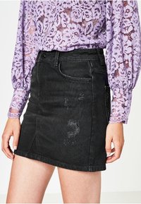 Svart denim mini kjol med en slitna design och subtil frans vid fållen. Har en standard femficklayout och bälteshål.