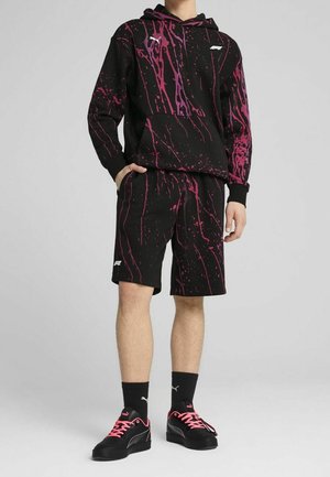 Person wearing black hoodie and shorts with pink splatter pattern, paired with black socks and black sneakers with pink laces.
