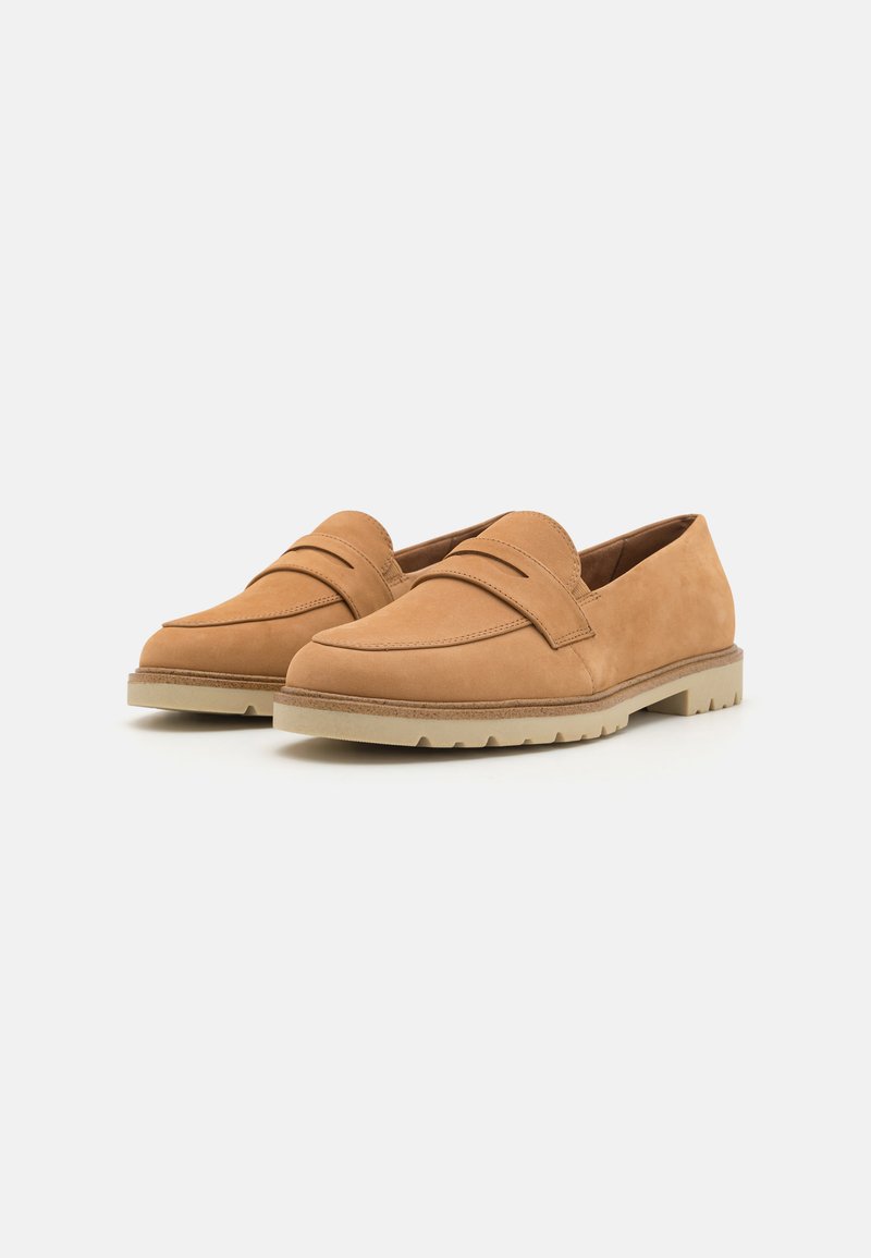 Mocassins en suède beige avec un bout arrondi, présentant un accent à double bride et une semelle en caoutchouc clair contrastante avec un motif de semelle.