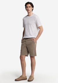 Vit t-shirt med kort ärm och beige shorts. Shorts har sidofickor och en främre dragkedja. Skorna är ljusbruna med en strukturerad yta.