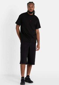 Zwarte katoenen t-shirt met ronde hals en korte mouwen, gecombineerd met zwarte shorts tot op de knie. Inclusief subtiele rode logodetail.