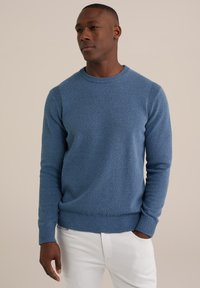 Suéter azul de punto con un acabado texturizado, cuello redondo y puños acanalados, combinado con pantalones blancos.