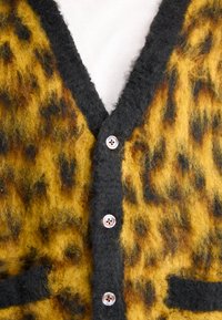 Κάρδιον με λεοπάρ σχέδιο σε κίτρινο και μαύρο μείγμα μαλλιού, με σκούρο γκρι γιακά, πέντε κουμπιά και δύο μπροστινές τσέπες.