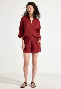 Rostfärgad, texturerad kortärmad skjorta med knappframsidan, matchad med shorts med elastisk midja. Svarta platta sandaler.