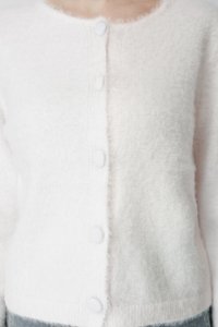 Κοντινή λήψη ενός ατόμου που φοράει ένα απαλό, λευκό, χνουδωτό πουλόβερ με κουμπιά πάνω από ανοιχτό μπλε τζιν.