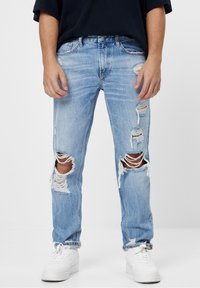 Ljusblå slitna jeans med revor vid knän och lår, fransiga kanter, vid passform, lätt blekning, kombinerade med vita sneakers, bomullsmaterial.