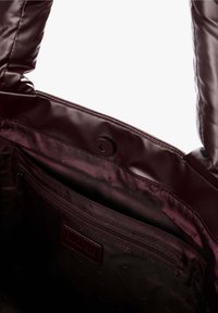Interno di una borsa a tracolla color marrone scuro che mostra una tasca con zip, foderato in tessuto con piccoli loghi ripetuti e chiusura a scatto magnetico nella parte superiore.