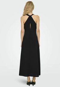 Crna maksi haljina s halter vratom. Ima otvorena leđa s detaljem u obliku ključanice i lepršavu, glatku tkaninu koja stvara elegantan siluetu.