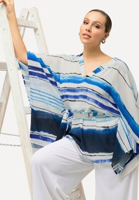 Top in stile kimono a strisce blu e bianche con scollatura a V, vestibilità ampia e cintura da annodare. Tessuto leggero, caratterizzato da linee orizzontali e tonalità variabili.