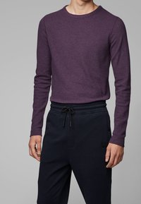 Långärmad t-shirt med rund hals i mörklila stickad tyg, ihopparad med svarta sweatpants med elastisk midja och sidofickor.