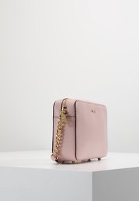 Rosa läderhandväska med en slät yta, rektangulär form, guldhardware, kedjehandtag och skyddande fötter i botten.