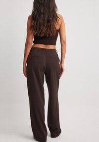 Bruine, wijde broek gemaakt van lichtgewicht materiaal met een soepele textuur. Bevat riemlussen en achterzakken.