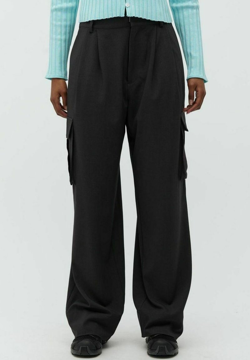 Schwarzfarbene Cargohosen mit weitem Bein aus Stoff, mit seitlichen Taschen und Falten. Kombiniert mit einer hellblauen gerippten Strickjacke.