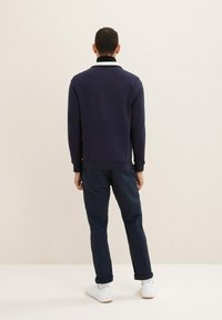Maglia a maniche lunghe blu navy con colletto in contrasto, abbinata a pantaloni tapered blu navy e sneakers bianche, che mostrano una vestibilità rilassata e una texture morbida.