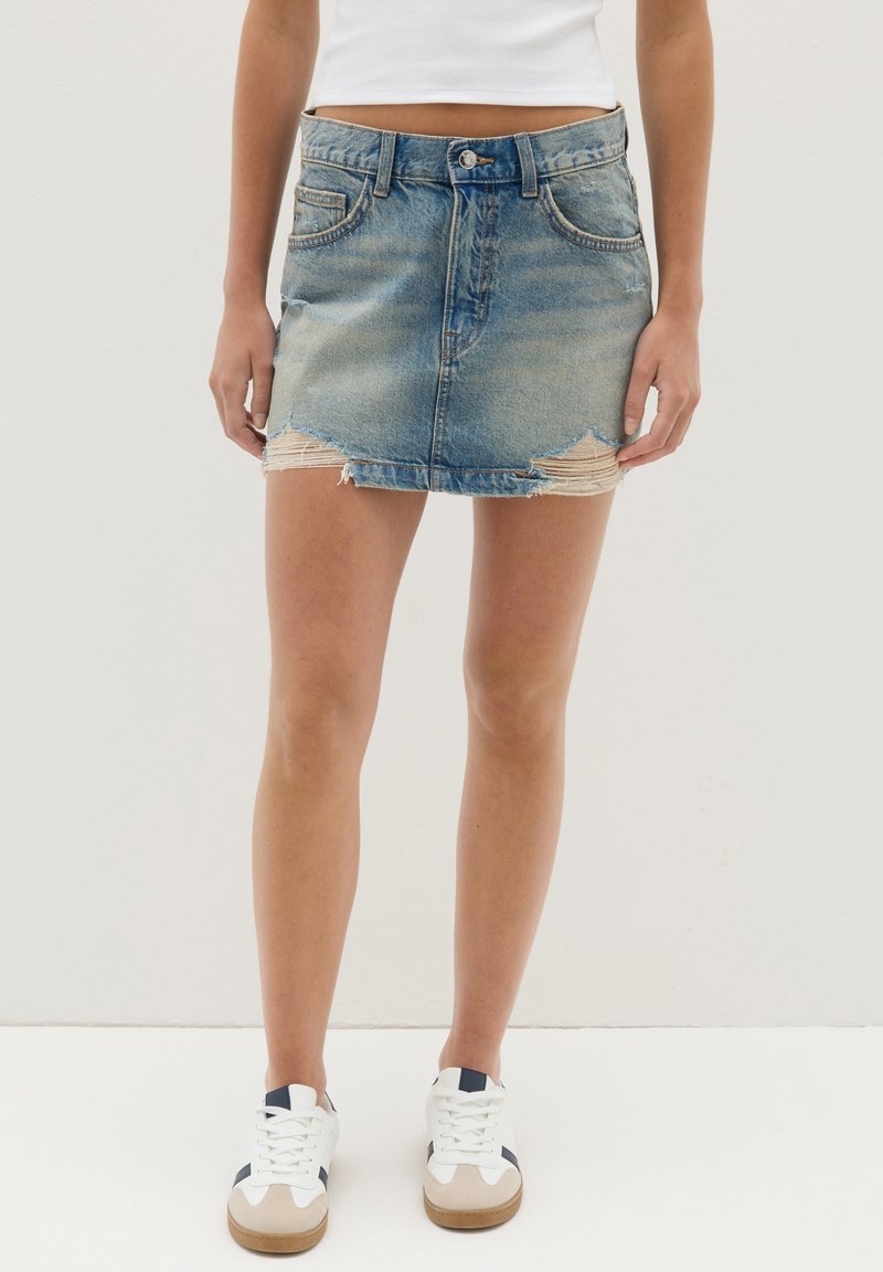 Hellblauer Denim-Minirock mit fransigem Saum und dezenter Ausbleichung. Verfügt über Fronttaschen und einen Knopfverschluss an der Taille.