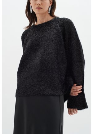 Maglione nero, texture morbida e dall'aspetto peloso, con una vestibilità ampia e maniche lunghe, abbinato a una gonna nera elegante. Il tessuto sembra soffice e piacevole al tatto.