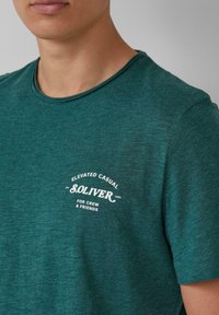 Teal casual t-shirt met een ronde hals. Bevat een witte geprinte logo en tekst, gemaakt van een gestructureerde, zachte stof.